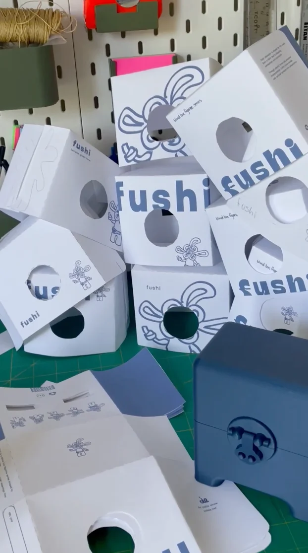 A pile of printed paper packaging iterations next to the blue box